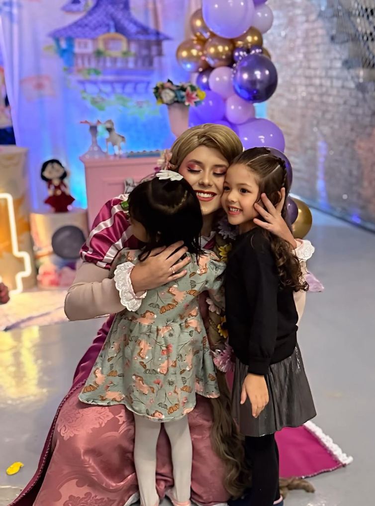 Personagem viva Rapunzel abraçando duas crianças em festa infantil